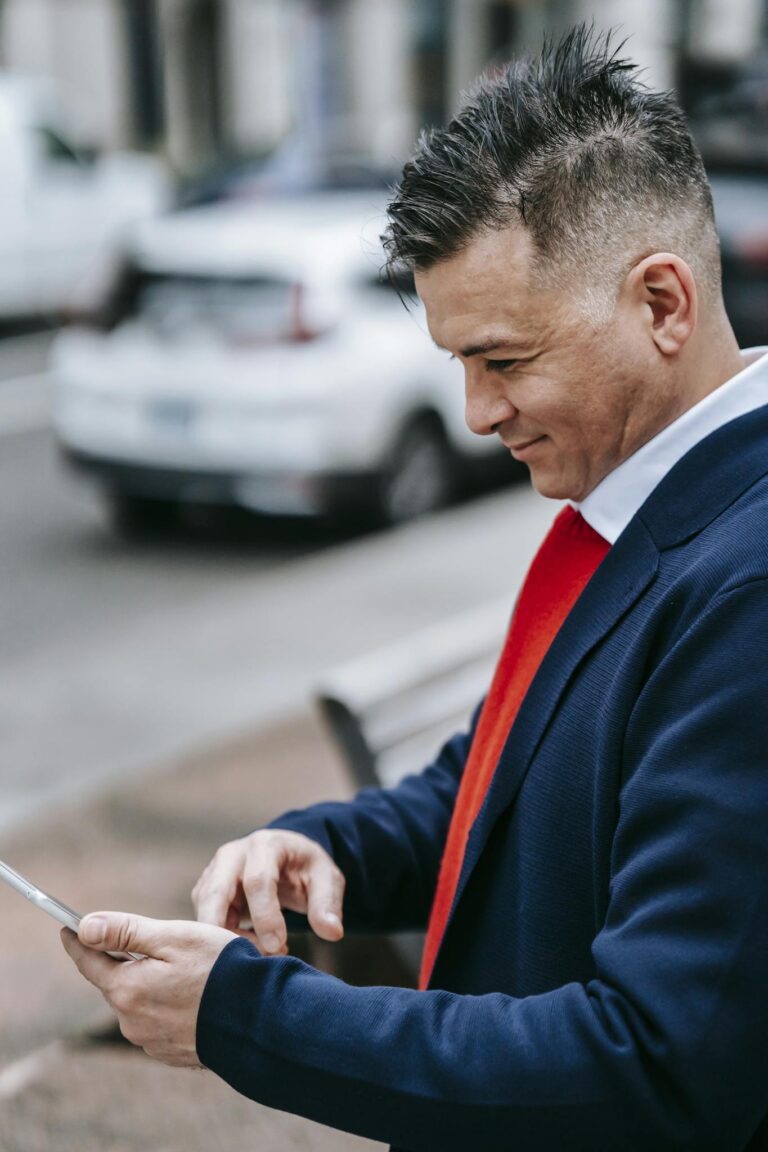 Stylish male professional using a tablet outdoors on a busy urban street.